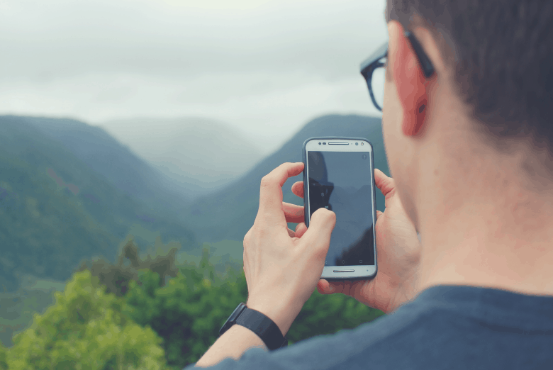 Man looking at phone with mountains in background